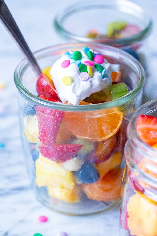 fruit salad in a cup topped with coconut whipped cream and sprinkles