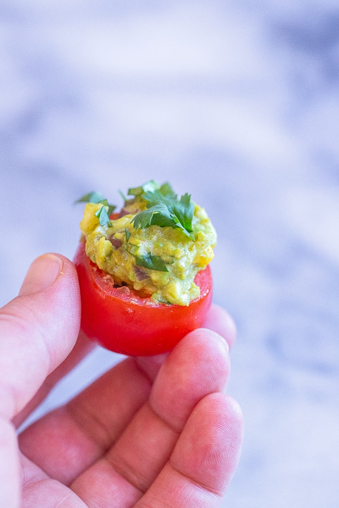 a hand holding a guacamole stuffed tomato