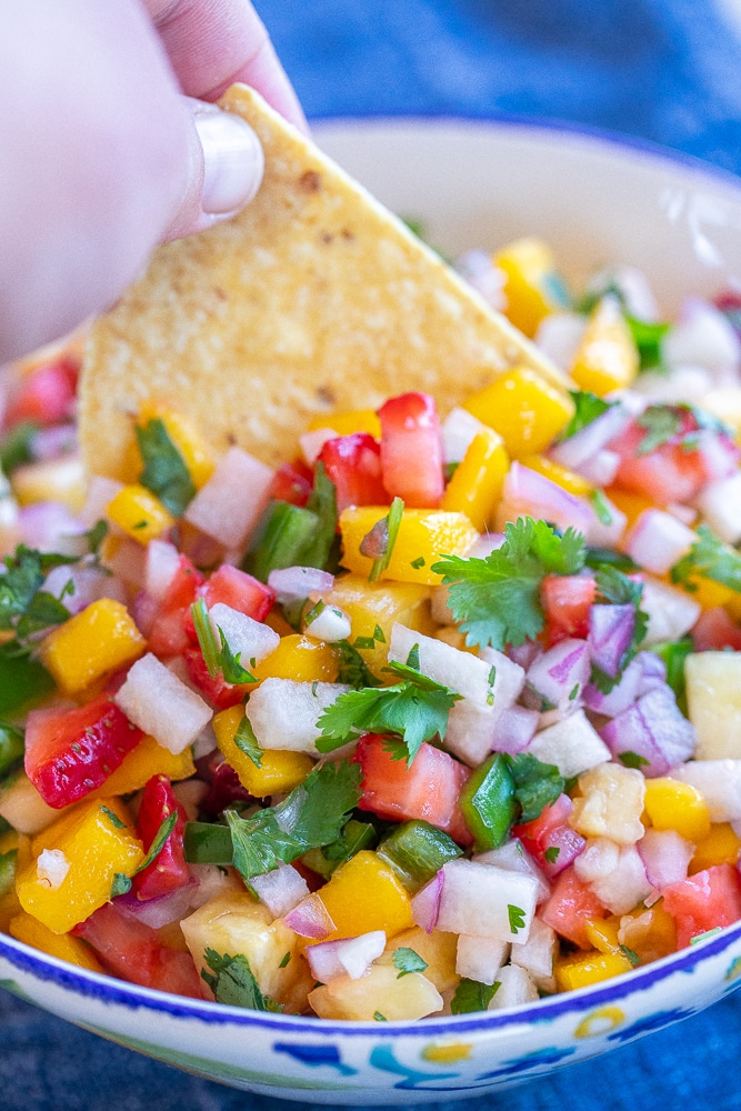 a chip being dipped into fruit salsa