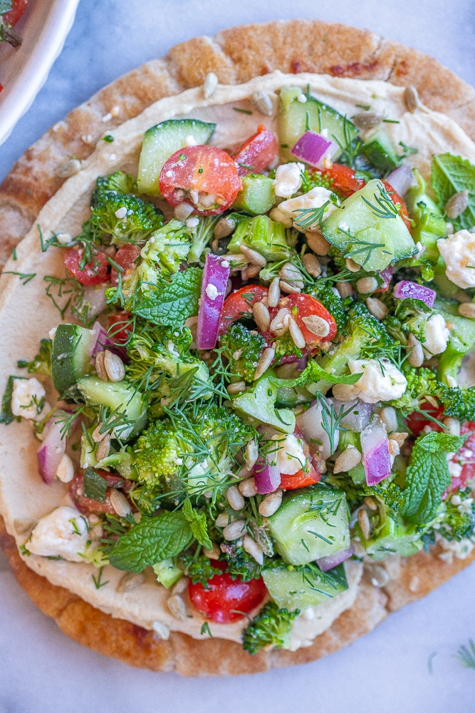 broccoli salad hummus pitas on a cutting board with fresh herbs