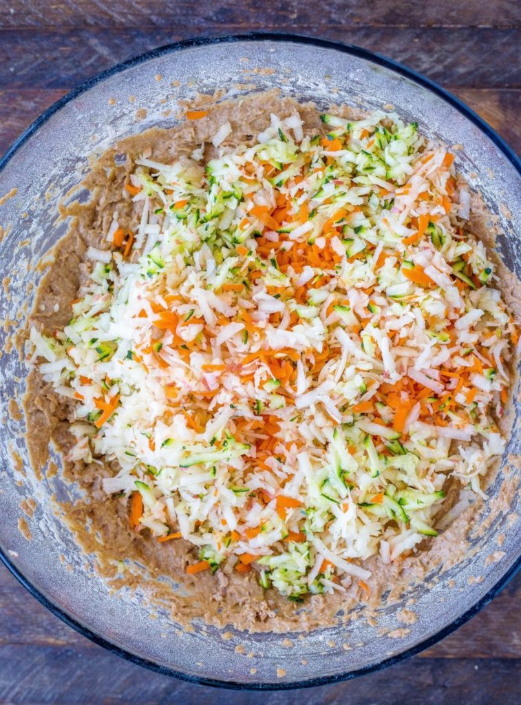 showing how to make zucchini apple carrot muffins with all the ingredients mixed in a bowl