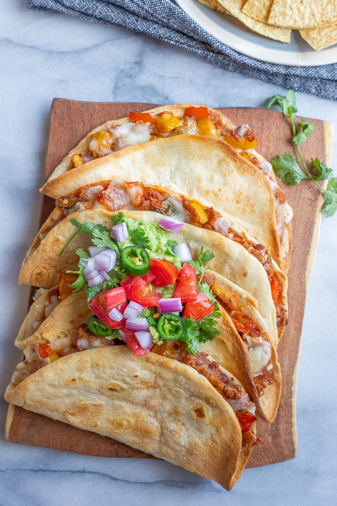 baked vegetarian tacos on a cutting board with toppings