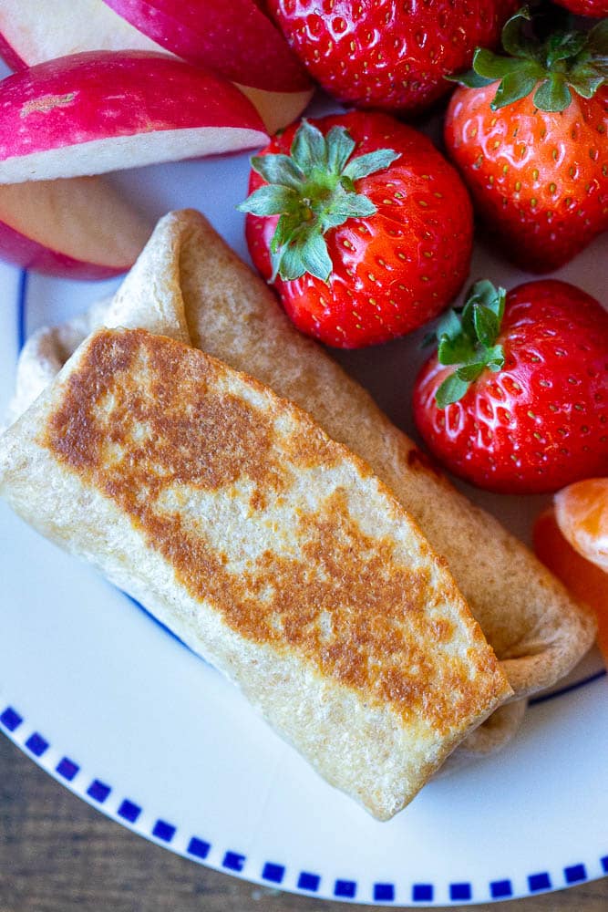 close up of a breakfast burrito on a plate with strawberries and apples