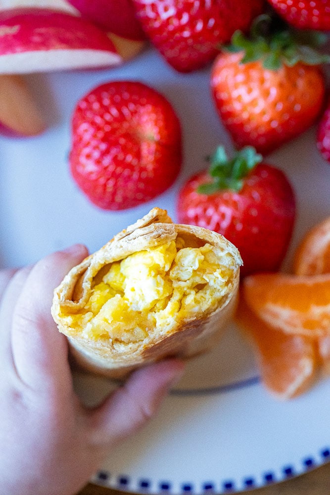 potato egg and cheese breakfast burrito in a child's hand with a bite taken out of it