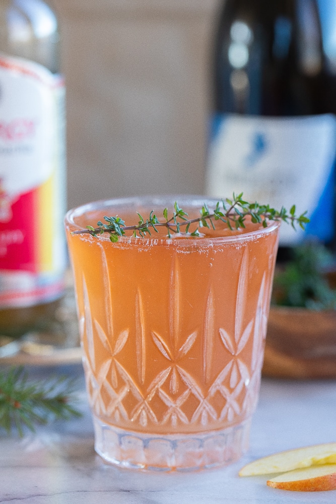 apple cranberry kombucha mimosa in a glass with some fresh thyme
