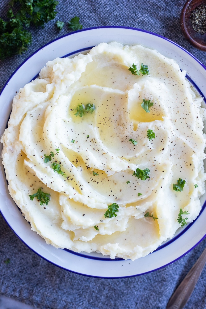 big bowl of creamy garlic herb butter mashed potatoes topped with pepper