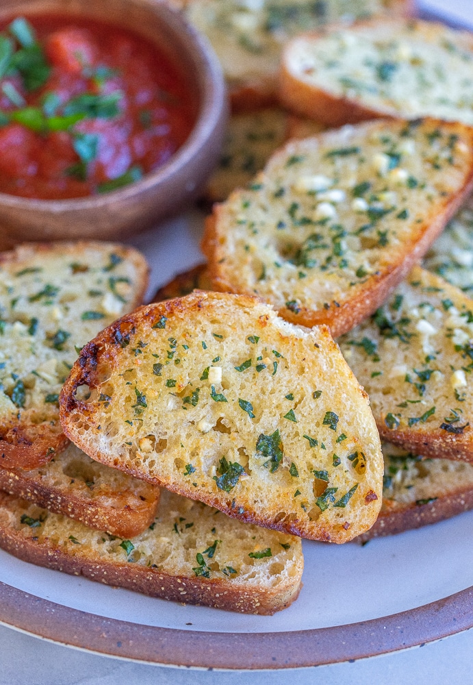 close up of a plate of thin and crispy garlic bread with dipping sauce