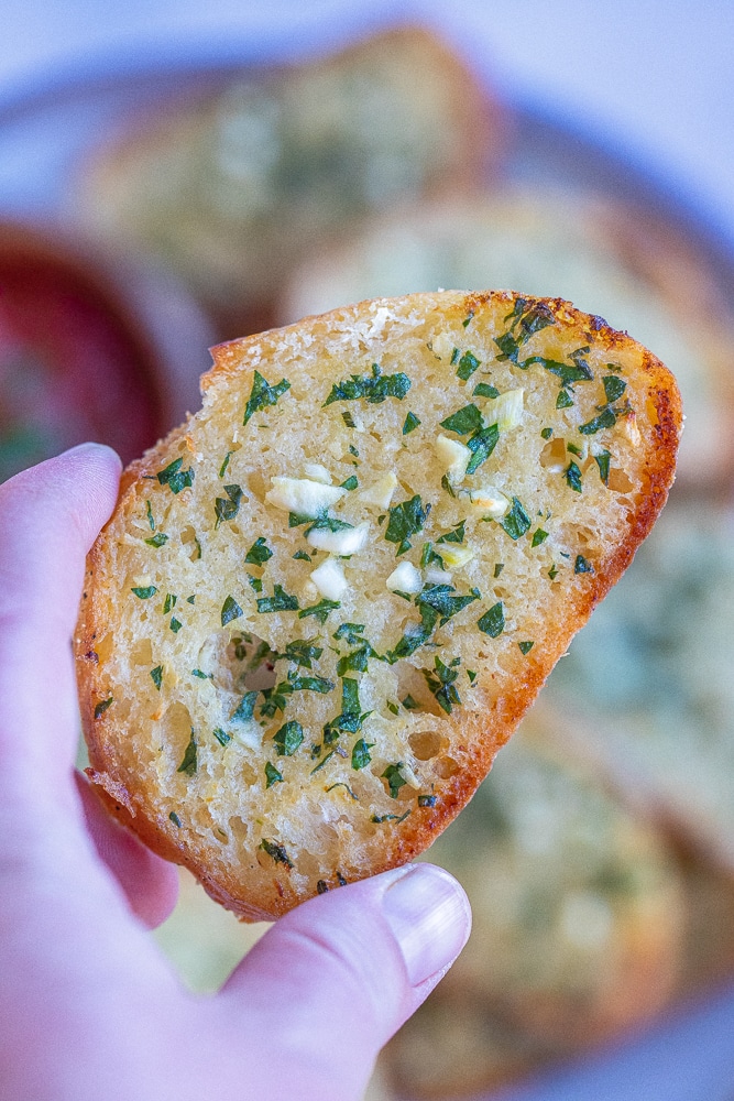 close up of a hand holding a slice of thin and crispy garlic bread