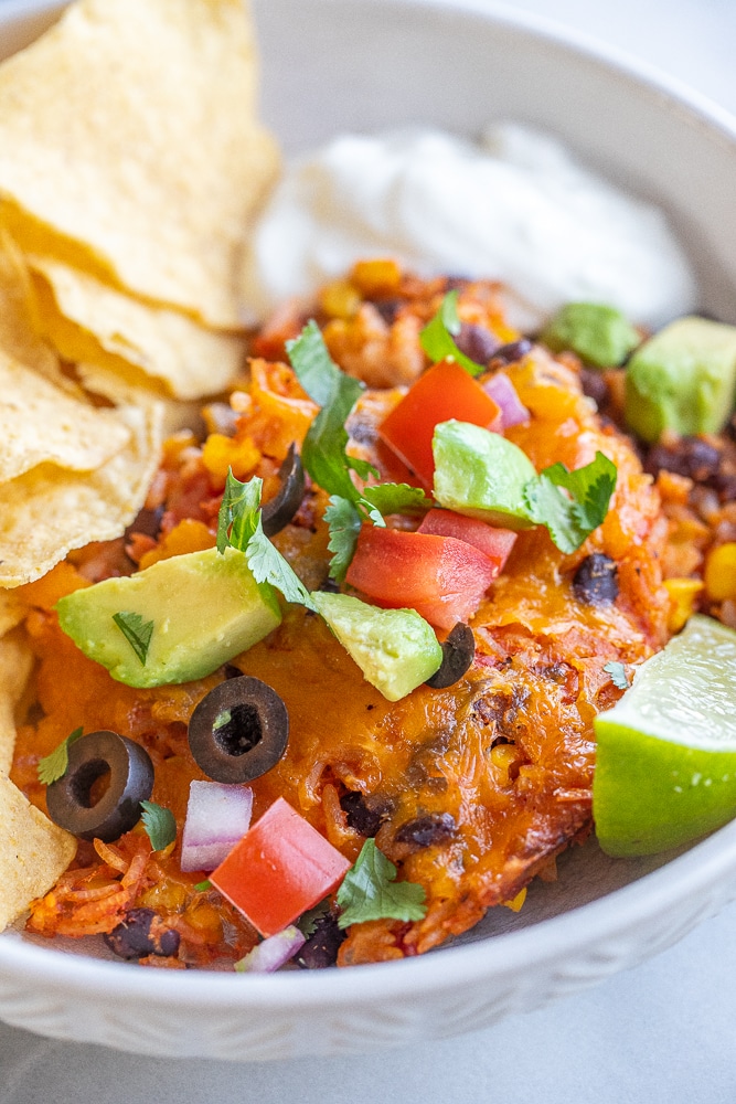 a serving of the rice and bean taco bake in a bowl with toppings and chips