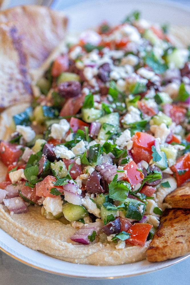 close up of a platter of greek salad on top of hummus