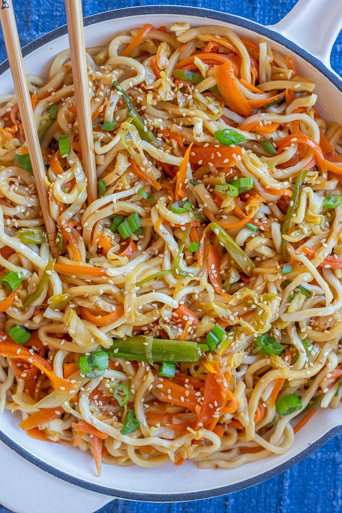 close up of noodles with cabbage and carrots in a frying pan with chopsticks
