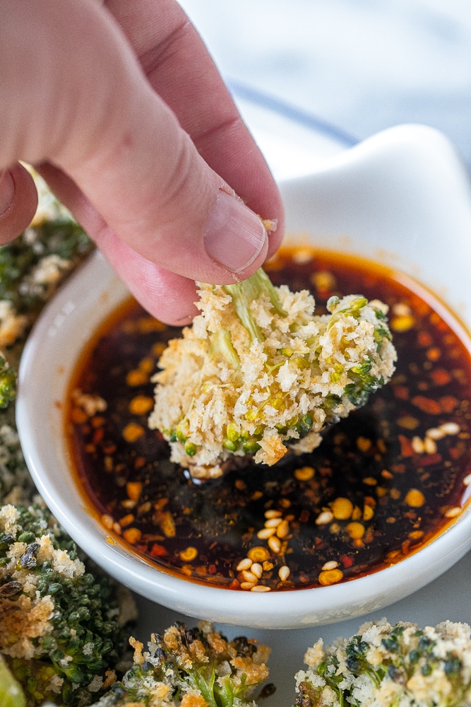 close up of panko coated broccoli being dipped into spicy soy sauce