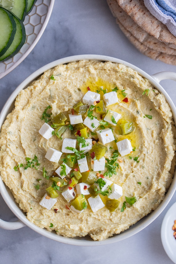 dill pickle feta hummus in a bowl with cucumbers and pita bread