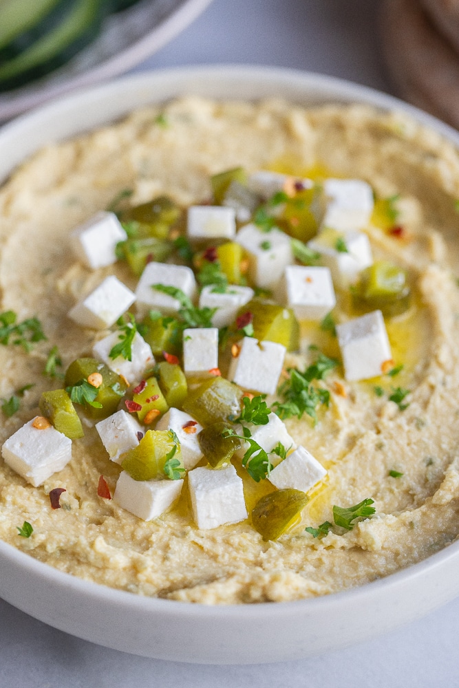 close up of dill pickle feta chickpea dip in a bowl with garnishes