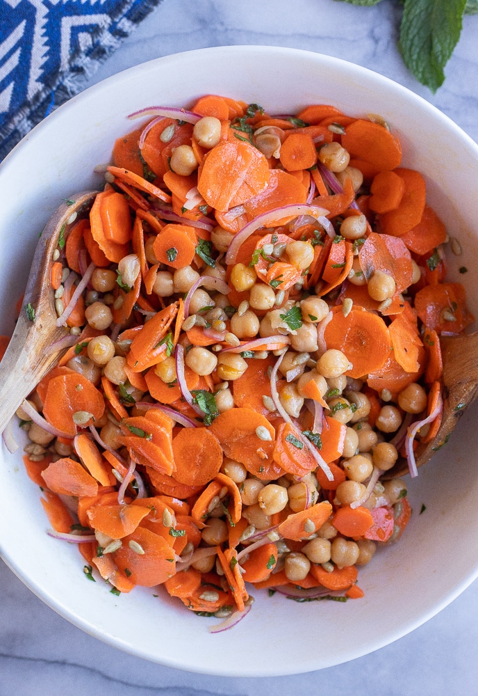 fresh carrot and chickpea salad in a bowl with a wooden spoon