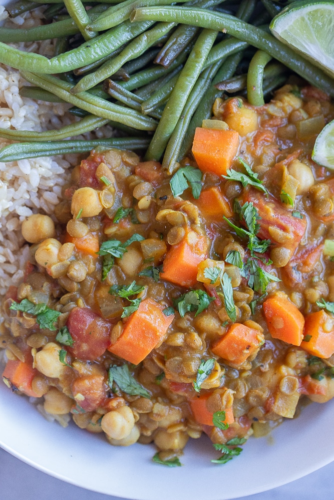 close up of lentil curry with carrots and chickpeas in a bowl with rice and green beans