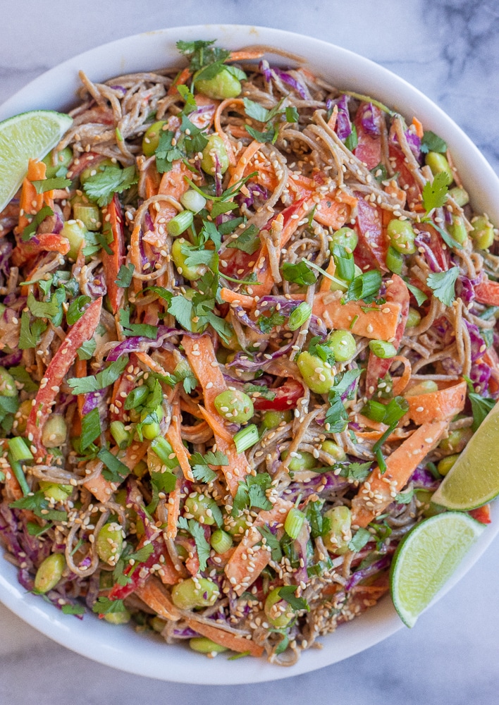 peanut soba noodle salad with vegetables in a large bowl with limes