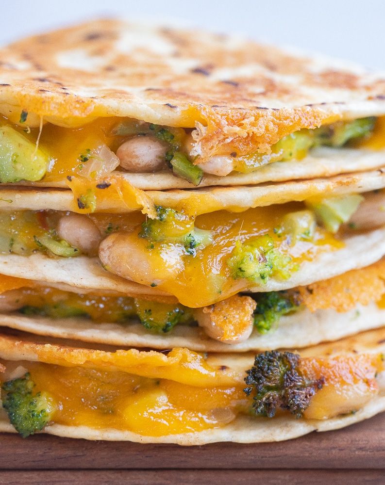 close up of cheesy broccoli quesadillas with white beans stacked on top of each other