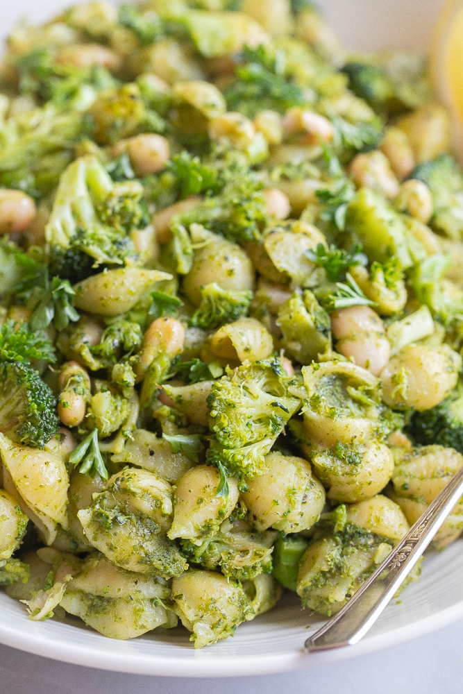 close up of a bowl of pesto pasta with broccoli and white beans