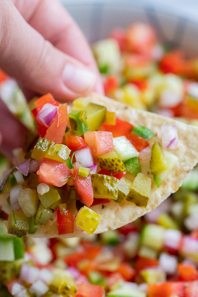 a hand holding a chip filled with pickle de Gallo