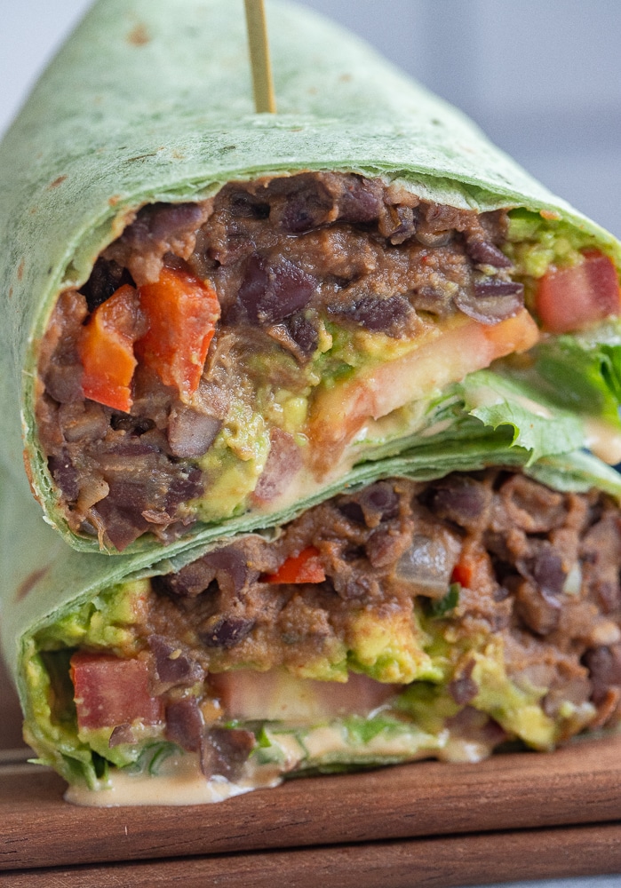 close up of a black bean wrap with chipotle tahini sauce stacked on top of each other