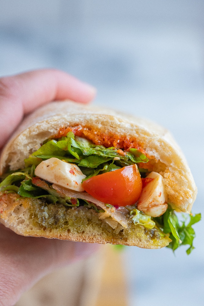 a hand holding a caprese sandwich with pesto