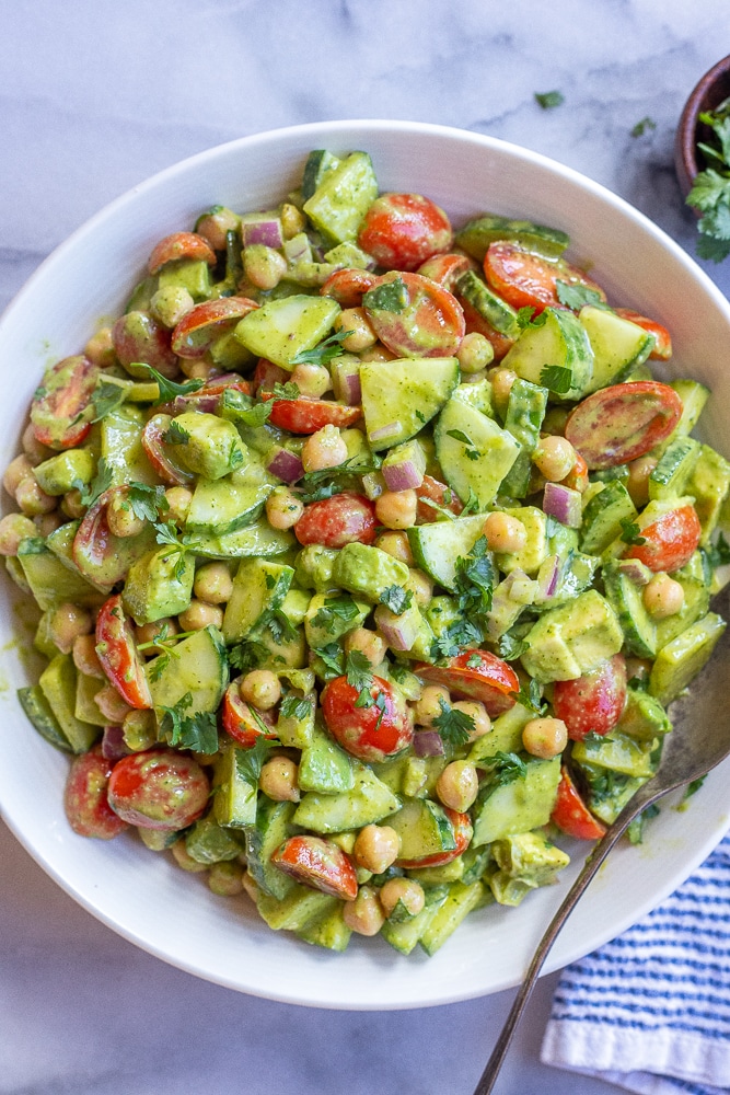 Cilantro Lime Cucumber Salad with Avocado and Tomatoes in a bowl with a serving spoon