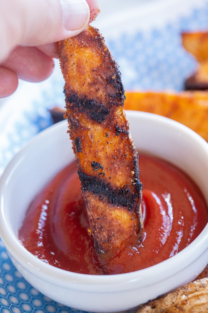 seasoned grilled potato wedge being dipped into a bowl of ketchup