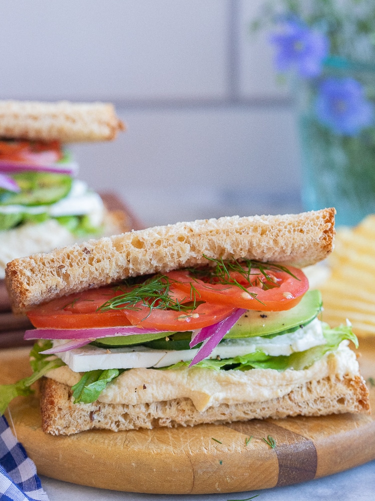 veggie sandwich with hummus on a cutting board with potato chips