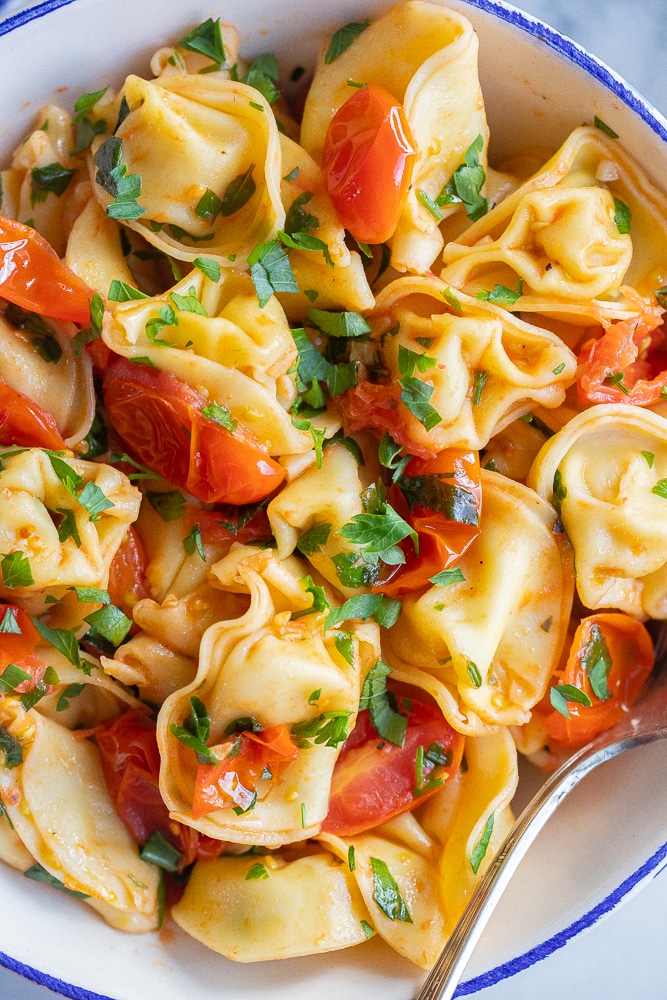 close up of cheese tortellini in a bowl with tomatoes and parsley