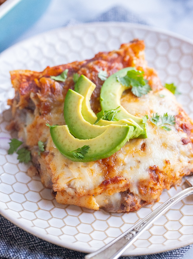 close up of a slice of bean and cheese enchilada casserole topped with avocado slices