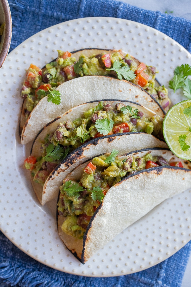 three vegetarian guacamole tacos on a serving plate with a lime
