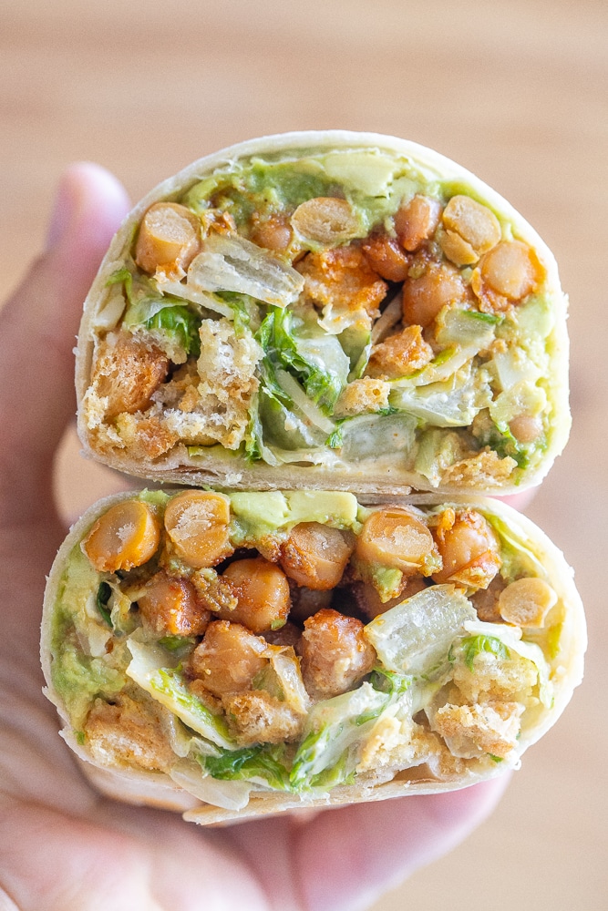 close up of a hand holding a chickpea Caesar salad wrap that has been cut in half
