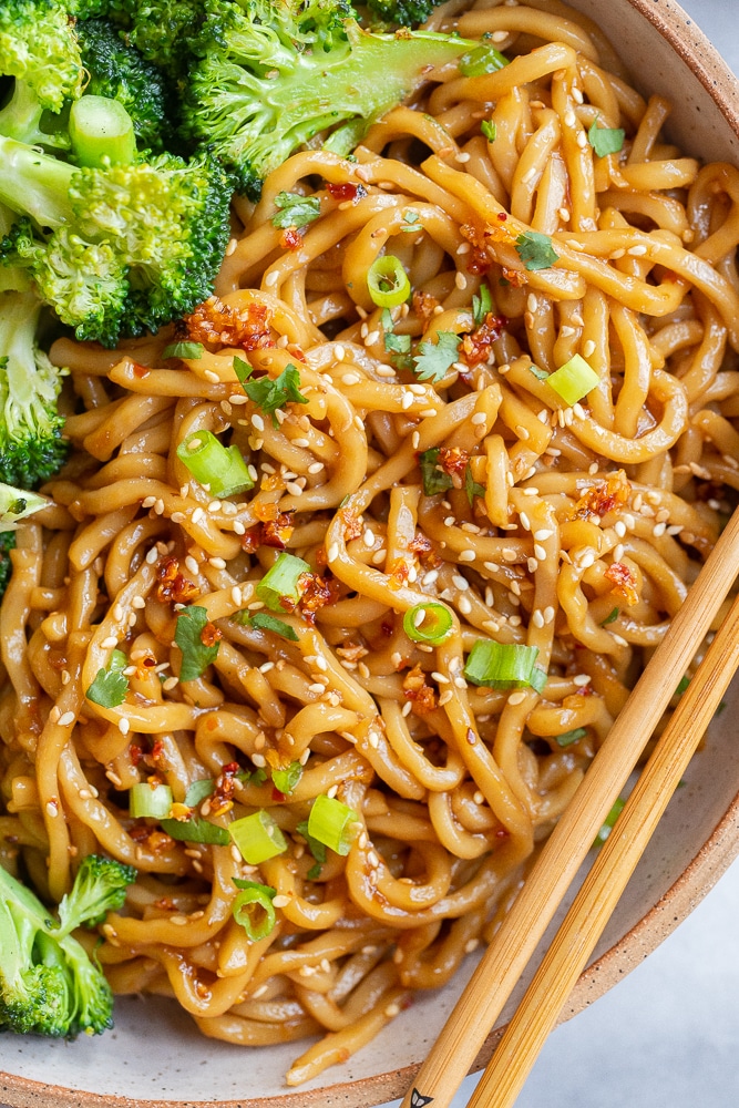 Close up of a bowl of sweet and spicy stir fry noodles with a side of broccoli