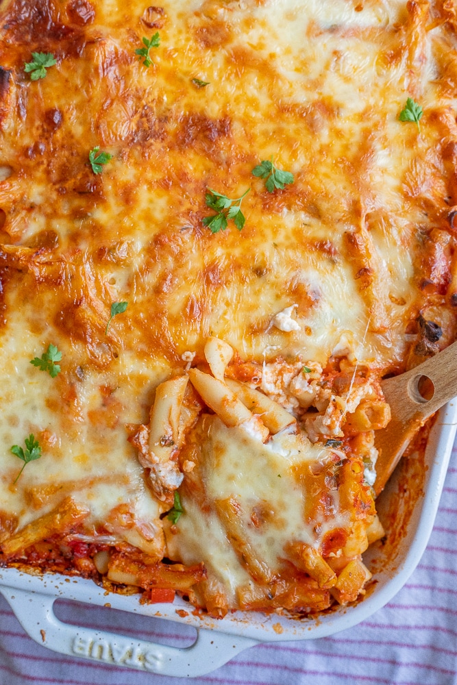 a pan of cheesy baked ziti with a wooden spatula
