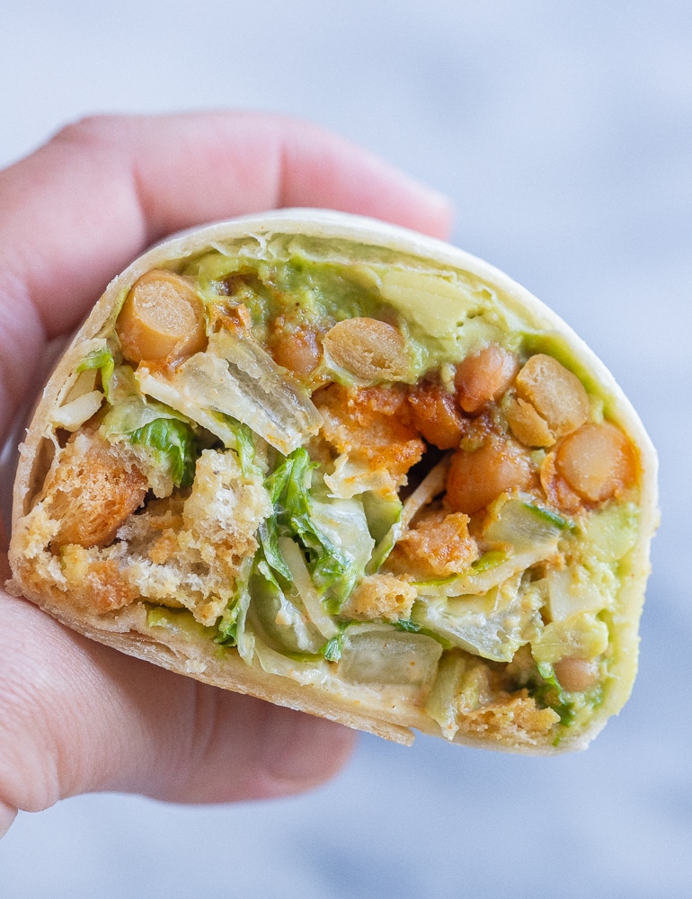close up of a hand holding a vegetarian chicken Caesar salad wrap that has been cut in half