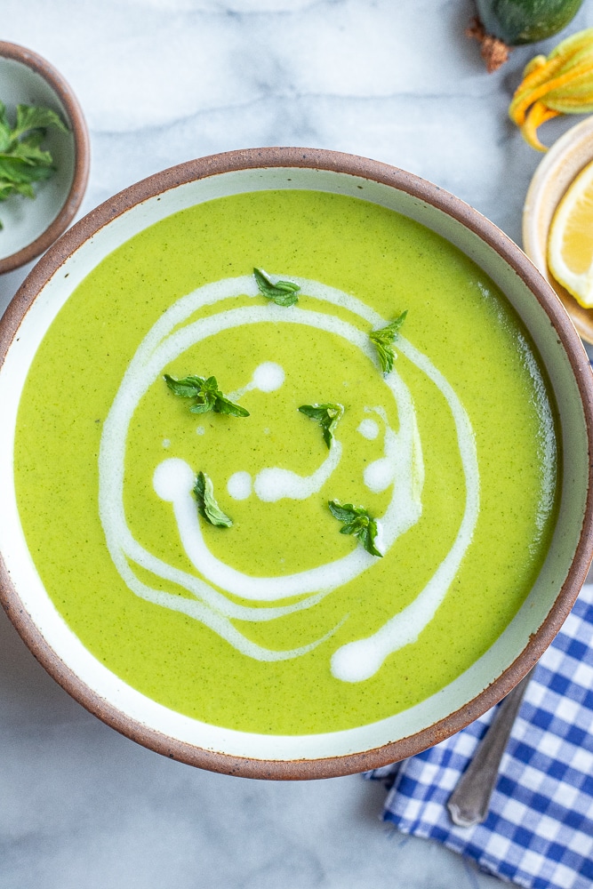 bowl of bright green curried zucchini soup with coconut milk swirled in