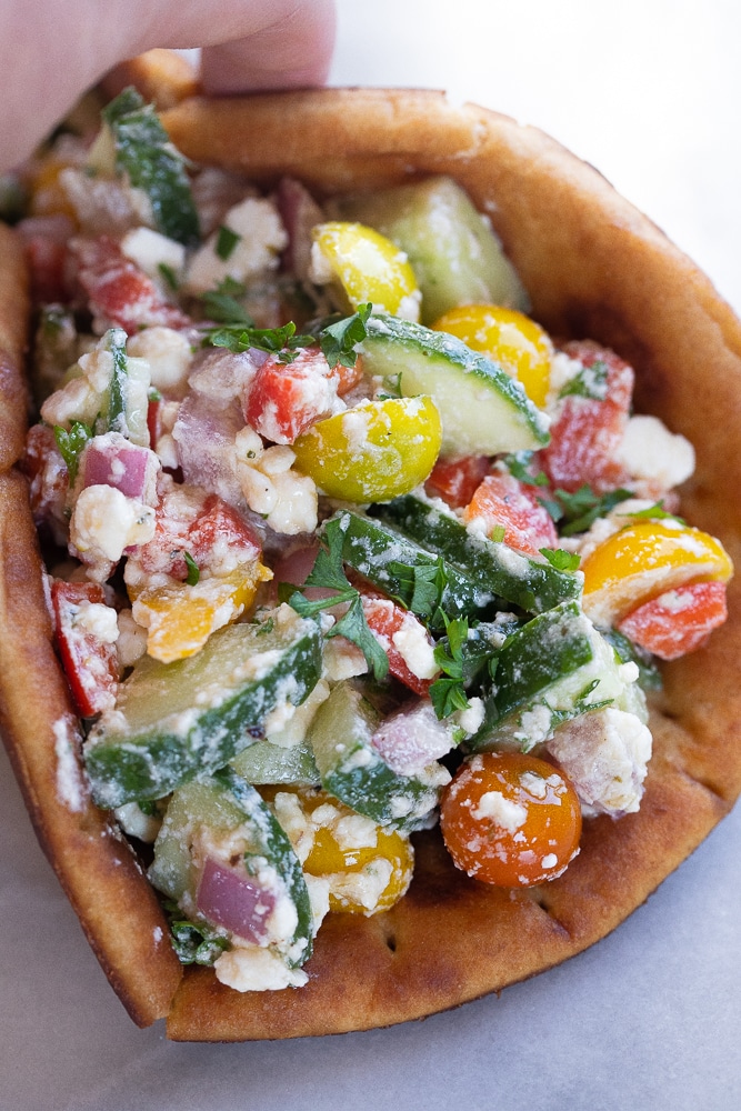 a hand holding a creamy feta and veggie pita wrap