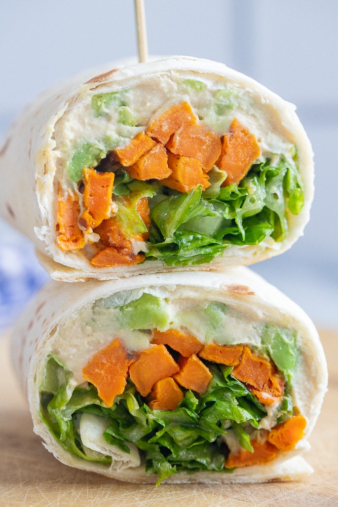 close up of a roasted sweet potato wrap with hummus cut in half on a cutting board