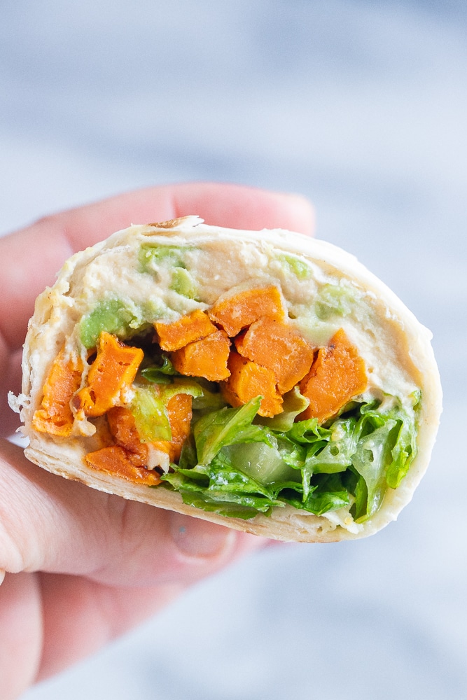 close up of a hummus wrap with roasted sweet potatoes cut in half being held by a hand