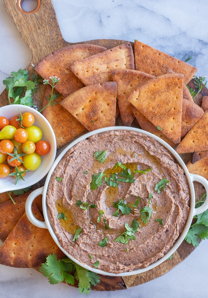 black bean hummus in a bowl on a platter with pita chips and cherry tomatoes