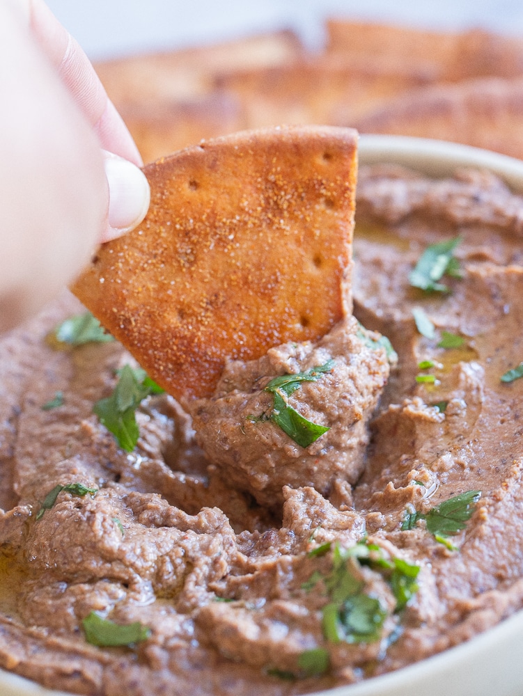 a pita chip being dipped into a bowl of spicy black bean hummus