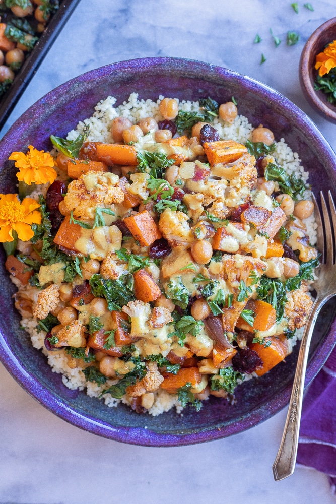 purple bowl filled with couscous and roasted veggies topped with tahini dressing