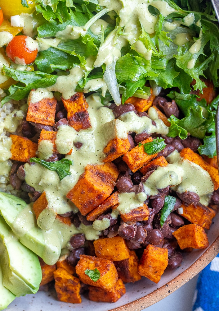 close up of seasoned roasted sweet potato with black beans and green tahini sauce