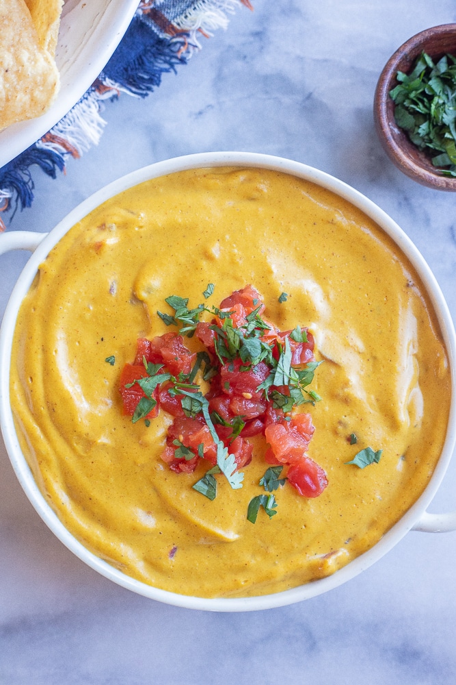 a big bowl of pumpkin queso dip with tomatoes and cilantro on top