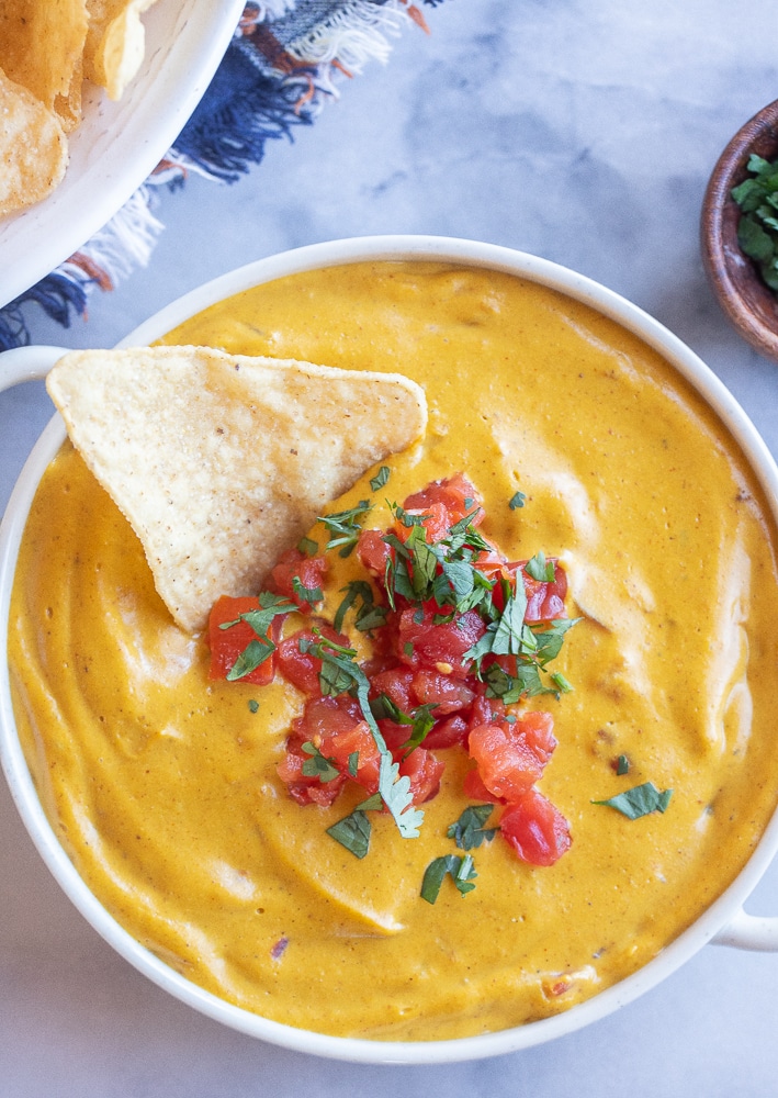 big bowl of vegan pumpkin cheese dip with chopped tomatoes and a chip in the bowl