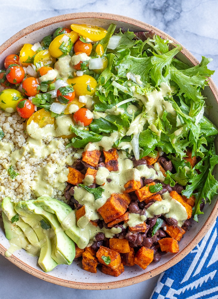 close up of a sweet potato quinoa bowl with green Chile tahini sauce drizzled over the top