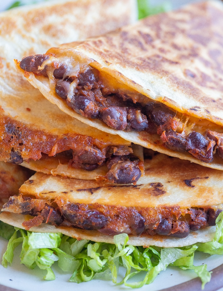 a stack of black bean quesadillas on a plate with lettuce