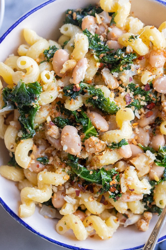close up of a bowl of cozy white bean and kale pasta with parmesan cheese