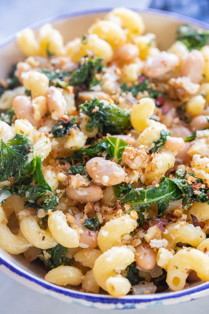 close up of pasta with white beans and kale in a bowl with parmesan cheese